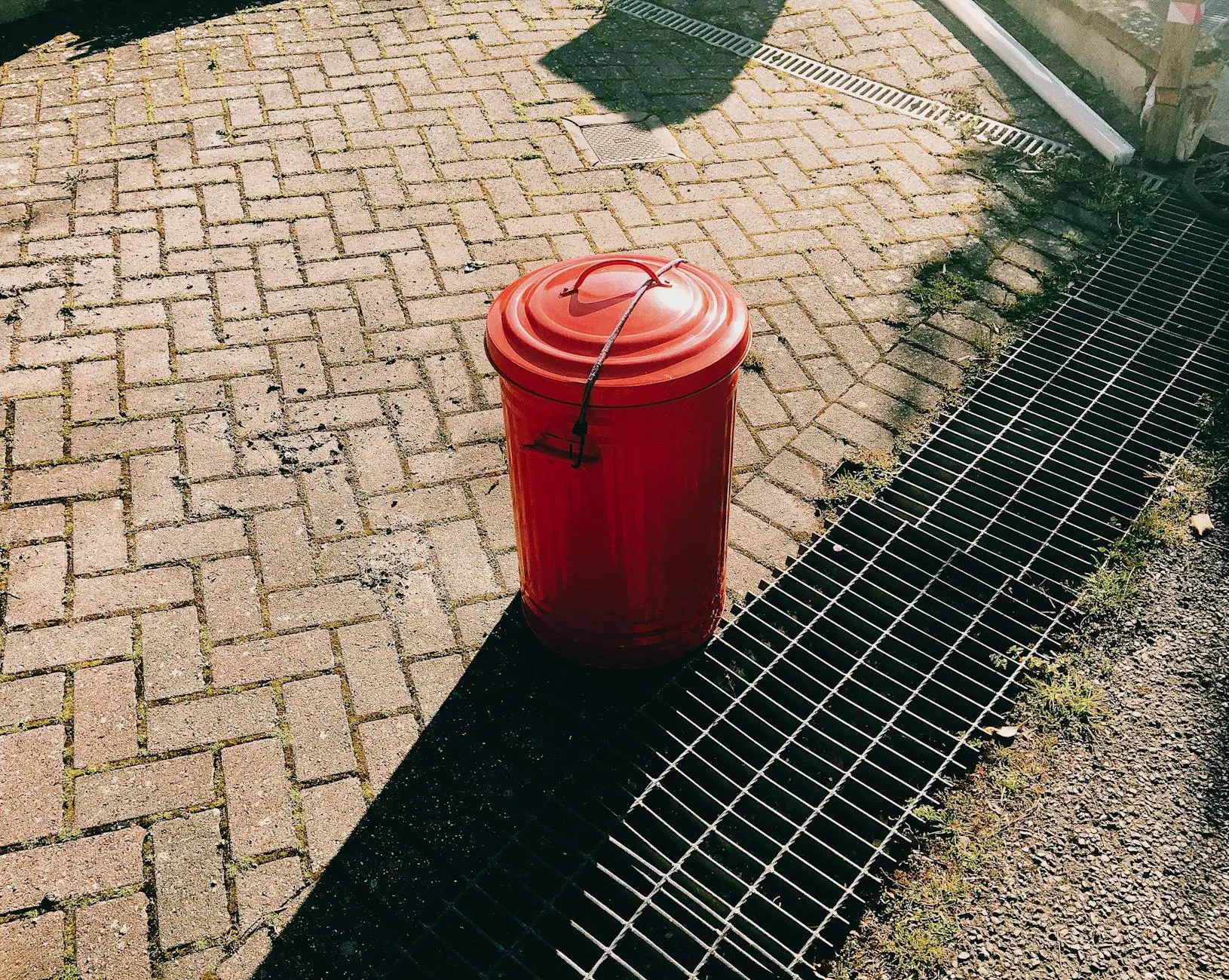 red trash can on pavement near sewer grates